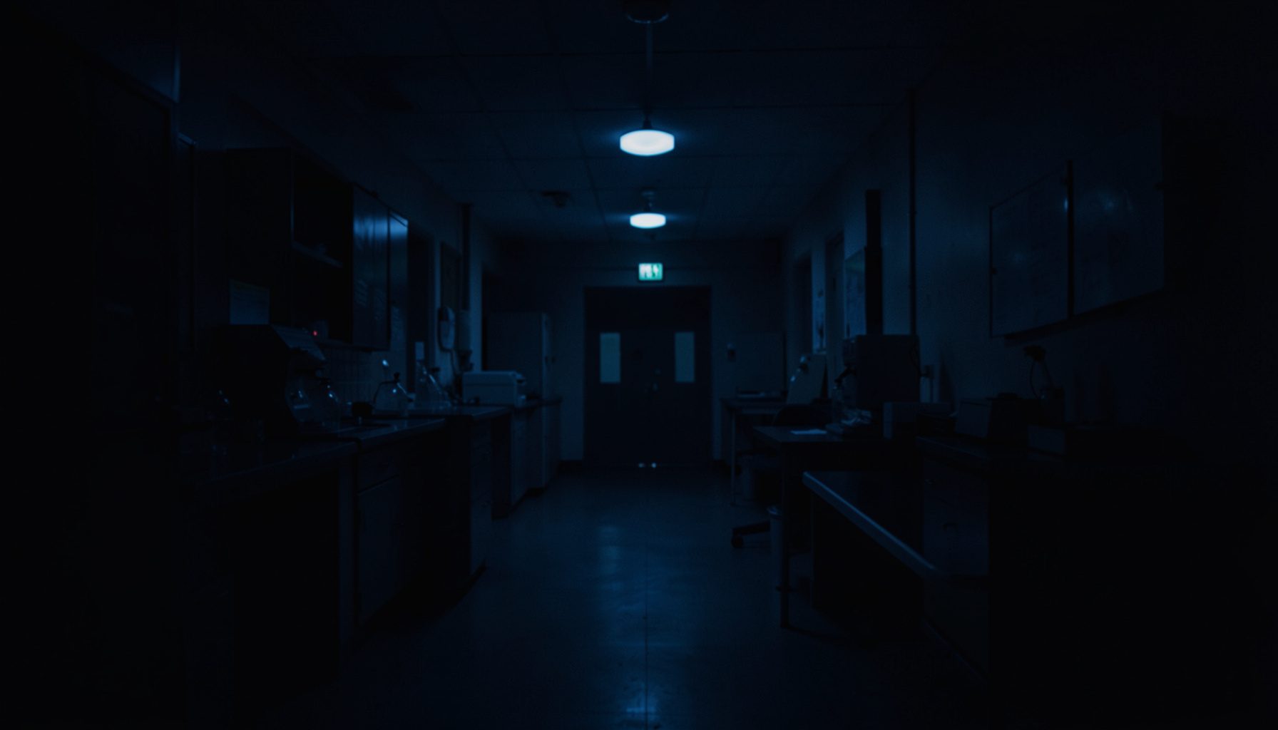 A dim, low-lit laboratory corridor with deep navy shadows and a faint glow from distant overhead lights, conveying a quiet and contemplative academic atmosphere.