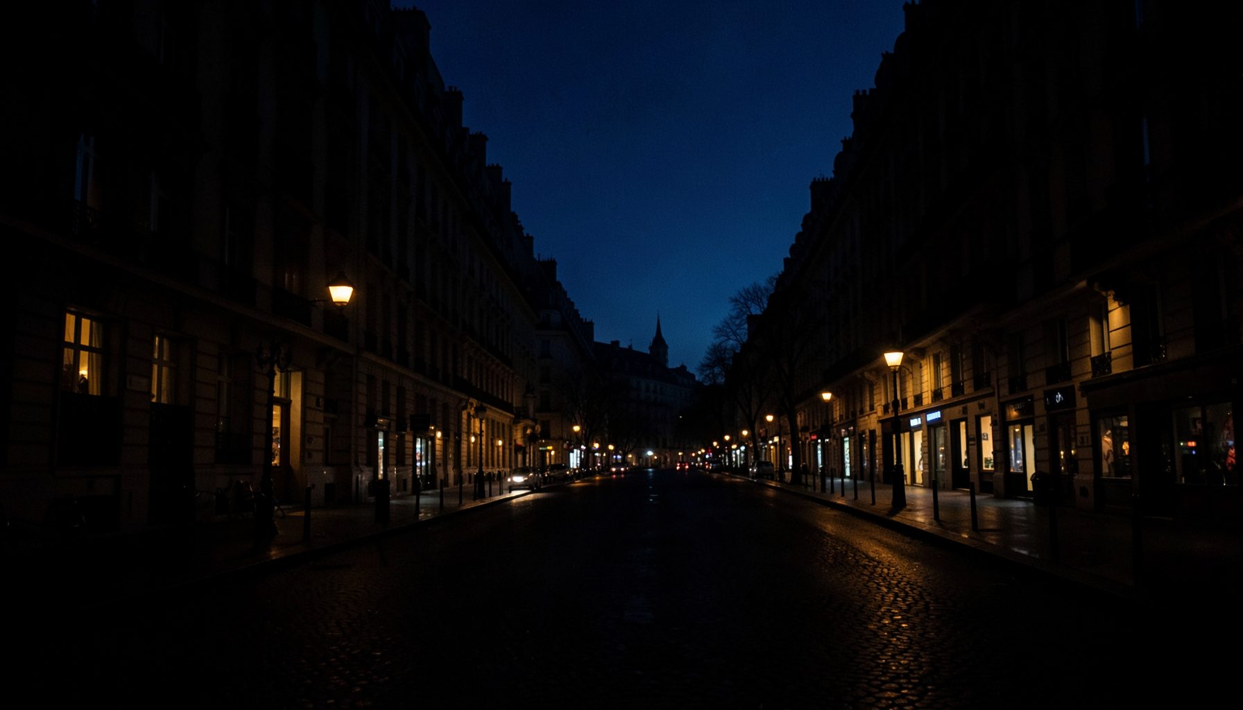 Dark, low-key evening photograph of a wide Parisian boulevard with warm lit windows receding into deep shadow