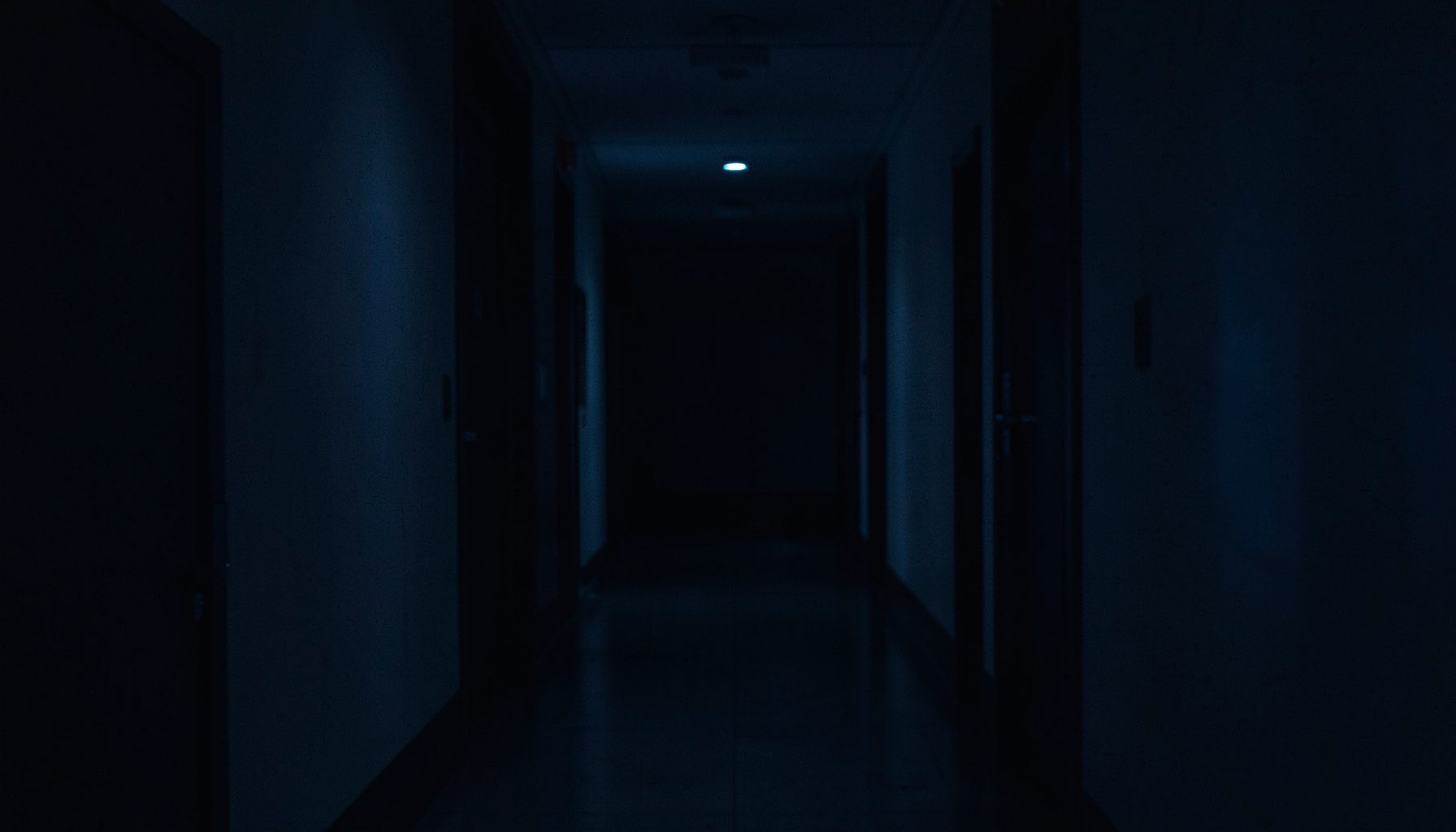 Dark, low-key photograph in deep navy and charcoal tones suggesting a quiet academic corridor with soft side lighting