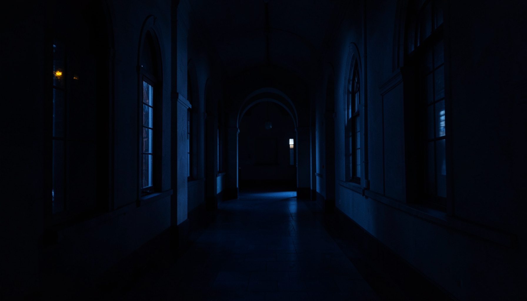 Dim, shadowy university corridor at night with tall arched windows, deep navy-blue tones and faint amber light, calm and academic